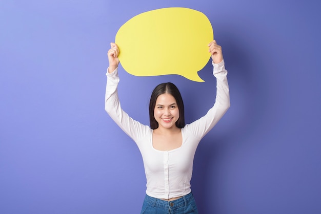 Photo young woman is holding yellow empty speech on purple background