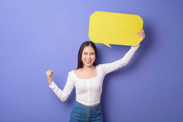 Young woman is holding yellow empty speech on purple background