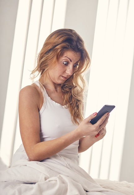 A young woman is looking at her smartphone in the morning, surprised