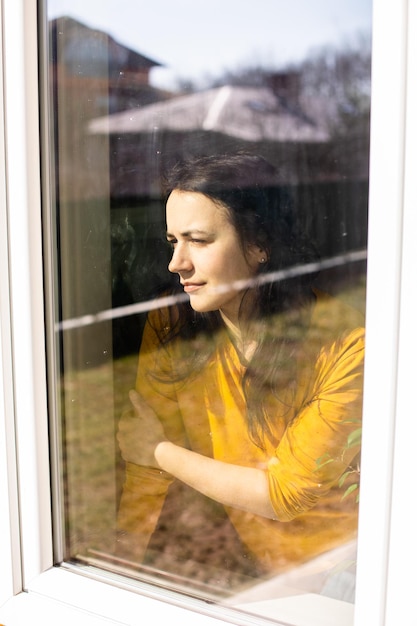 Молодая женщина смотрит в окно в солнечный день