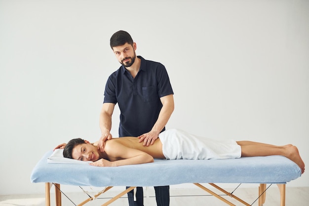 Young woman is lying down when man doing massage of her body at spa