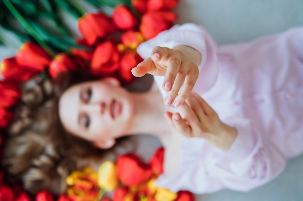 A young woman is lying on the floor among red tulips The concept of March 8 Valentine's Day Spring portrait of a womanFocus on the girl's hands in the foreground