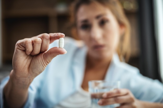 Young woman is lying sick at home couch and taking pills. Selective focus.