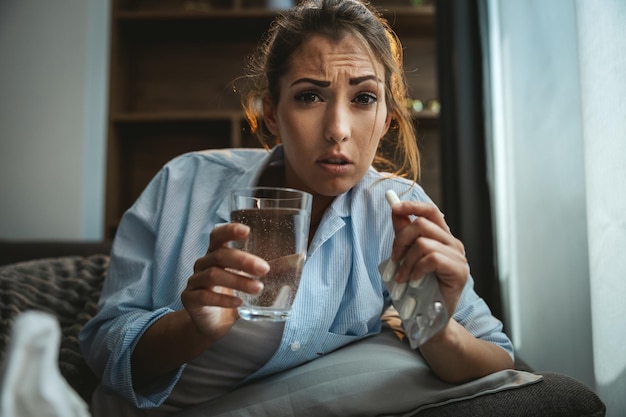 Young woman is lying sick at home couch and taking pills.