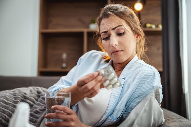 Young woman is lying sick at home couch and taking pills.