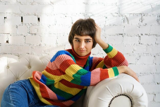 A young woman is lying on a sofa in a multicolored sweater and socks