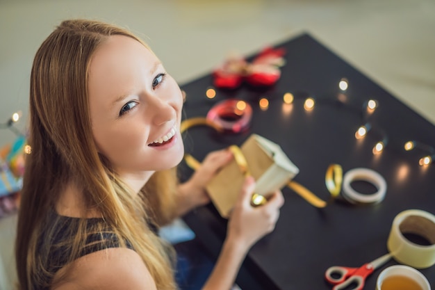 La giovane donna sta imballando i regali. regalo avvolto in carta artigianale con un nastro rosso e oro per natale