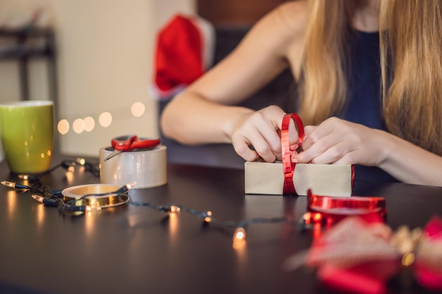 Young woman is packing presents present wrapped in craft paper with a red and gold ribbon for