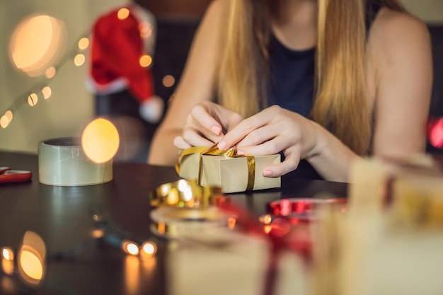 Young woman is packing presents present wrapped in craft paper with a red and gold ribbon for