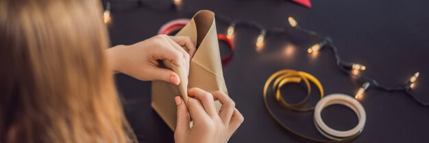 Young woman is packing presents present wrapped in craft paper with a red and gold ribbon for