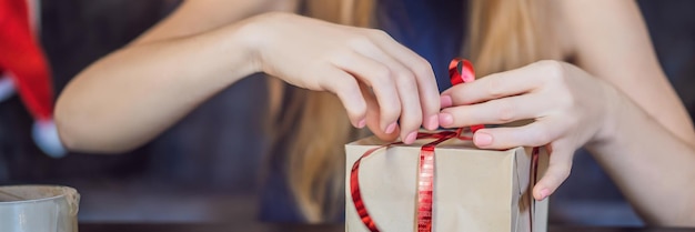 사진 젊은 여성이 빨간색과 금색 리본이 달린 공예 종이로 포장된 선물 선물을 포장하고 있습니다.
