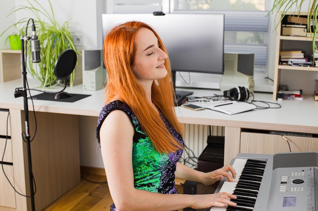 The young woman is playing in the studio on a synthesizer