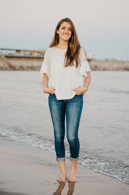 A young woman is posing on a sandy beach near water at twilight in Spain