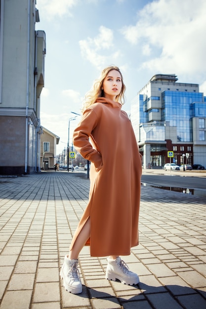 Young woman is posing in a warm light brown dress on a street