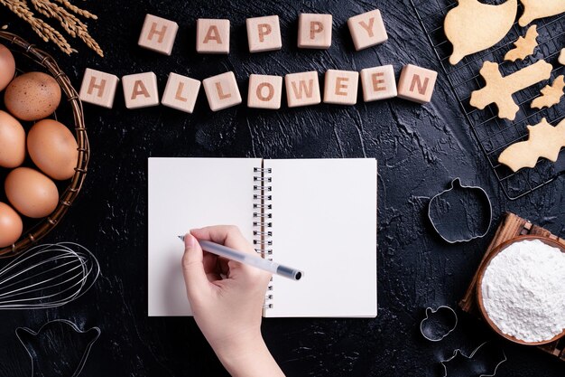 Young woman is reading and writing recipe of making Halloween cookies design concept of preparing for Halloween party top view flat lay overhead