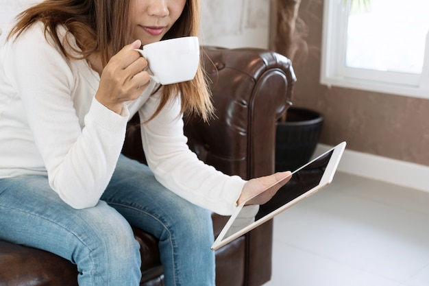 Young woman is relaxing on comfortable couch and using tablet at home.	
