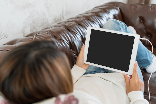 Young woman is relaxing on comfortable couch and using tablet at home.