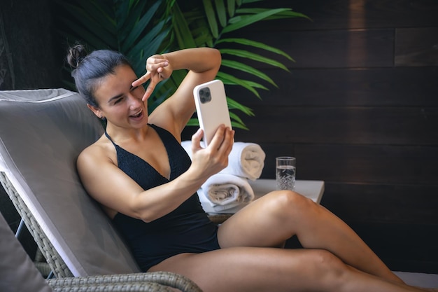 A young woman is relaxing in a spa complex and using a smartphone