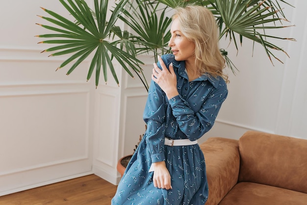 young woman is resting in a beautiful feminine blue dress in a bright room by the window relax