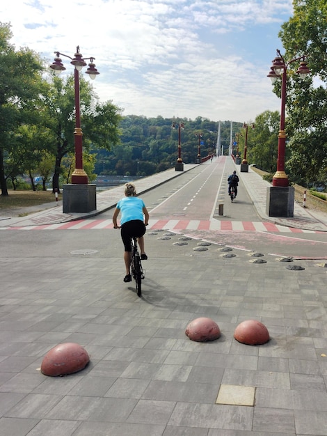 若い女性がアスファルト道路に沿って自転車に乗って橋に着く自然の中のアクティブなレクリエーション