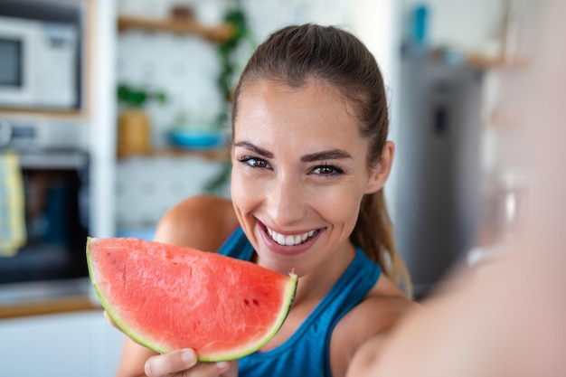 A young woman is seen in her kitchen happily savoring a slice of juicy watermelon Her expression reflects pure enjoyment as she takes each bite embodying the simple pleasure of the moment