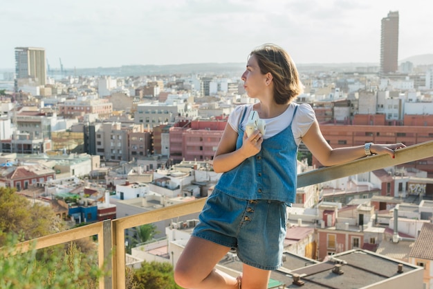 Young woman is shooting with a instant camera with the city of Alicante