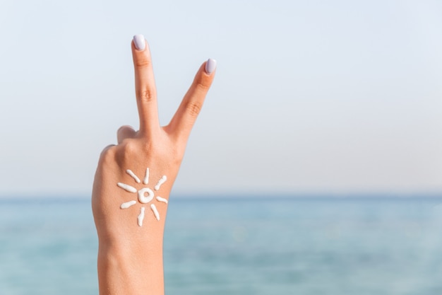 Young woman is showing peace gesture and has sun shape on her hand at the beach.