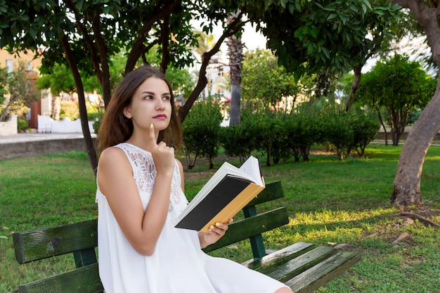 Молодая женщина сидит на скамейке в парке и думает о том, что она прочитала