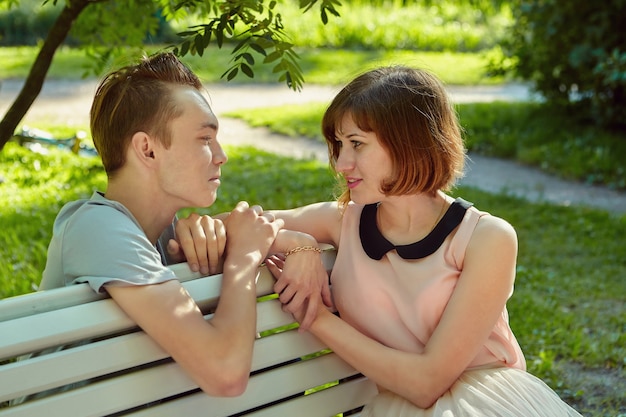 Young woman is sitting on bench in public park with her lover near during their meeting.