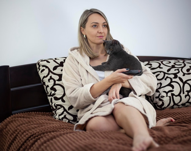 Foto una giovane donna è seduta sul divano con il suo gatto in grembo nel salotto e guarda la tv.