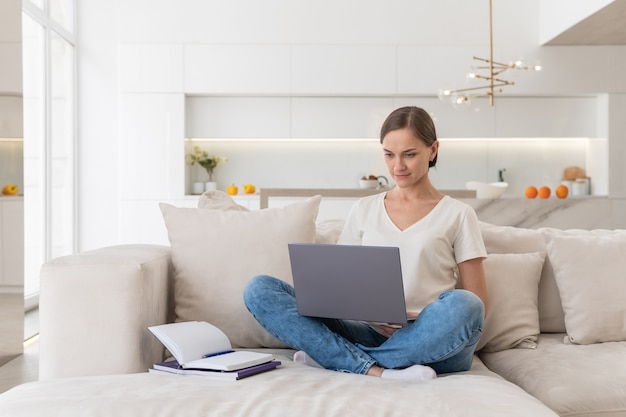 Young woman is sitting on the couch and working on a laptop