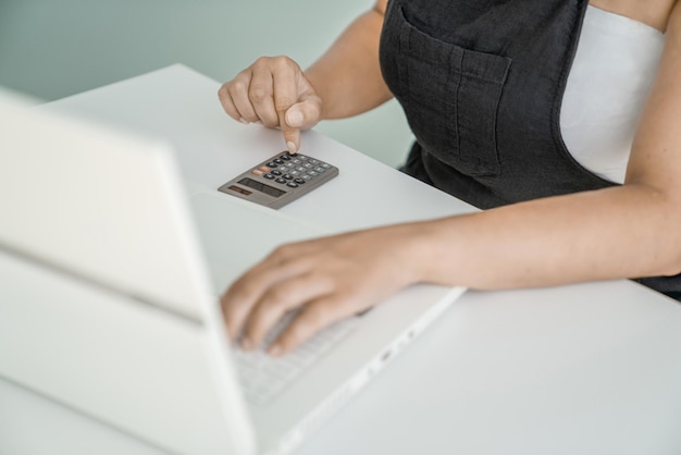 Young woman is sitting at her laptop and doing calculations on calculator closeup