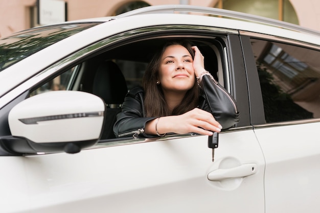 若い女性が彼女の新しい車に座って、成功した実業家の鍵を握っています