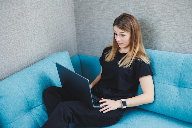 A young woman is sitting on a sofa and working on a laptop Remote work Work at home online