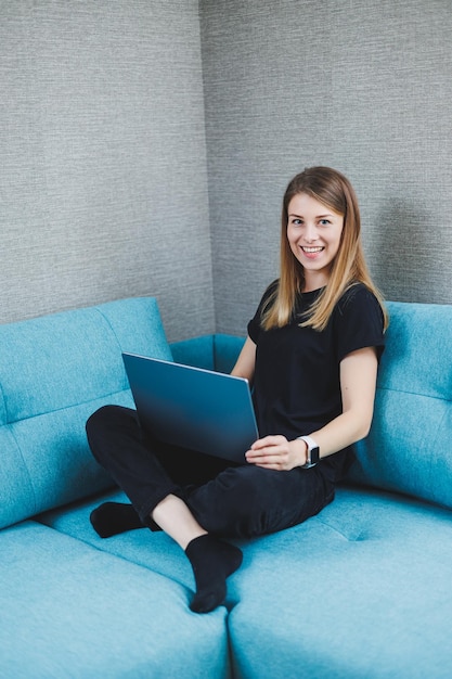 A young woman is sitting on a sofa and working on a laptop Remote work Work at home online