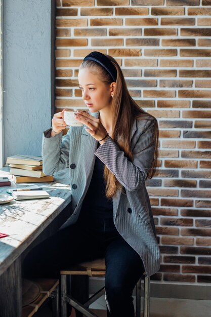 Foto una giovane donna è seduta a un tavolo vicino alla finestra in un caffè e beve caffè