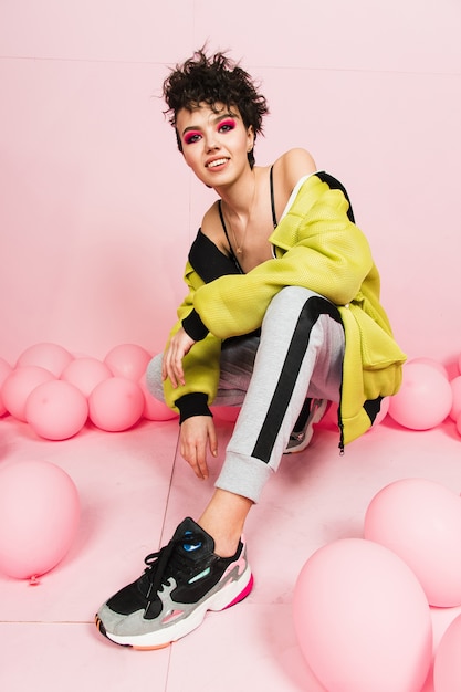 A young woman is smiling at the camera. Sitting in a yellow sweater and sneakers