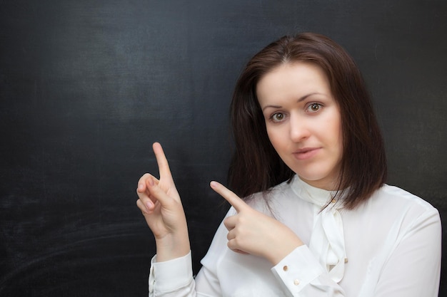 Young woman is smiling and pointing up, against black chalkboard