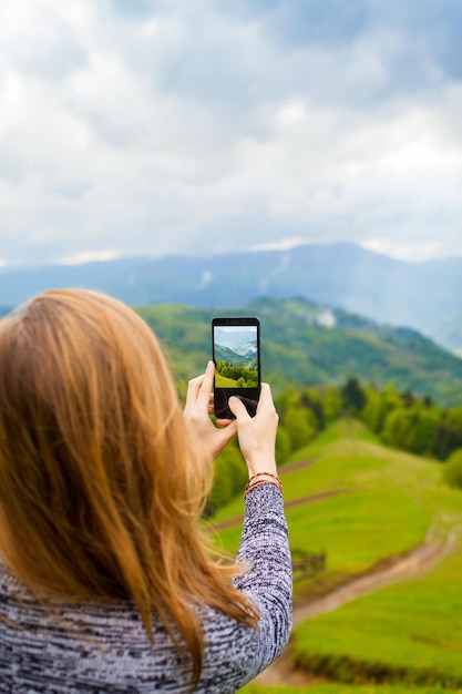 Foto la giovane donna è in piedi sulla collina e sta scattando foto di uno splendido paesaggio con foreste di montagna e cielo nuvoloso