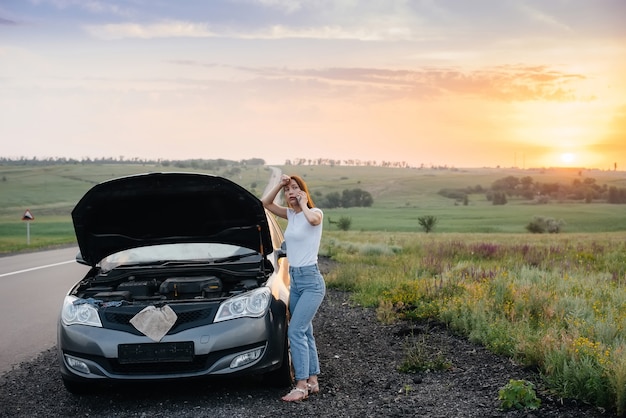 A young woman is standing near a broken-down car.

