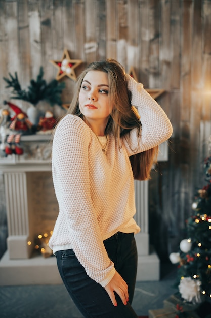 Young woman is standing near the Christmas tree and fireplace in the room