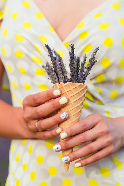 Young woman is standing with lavender flowers in a waffle cup holding in a hand.