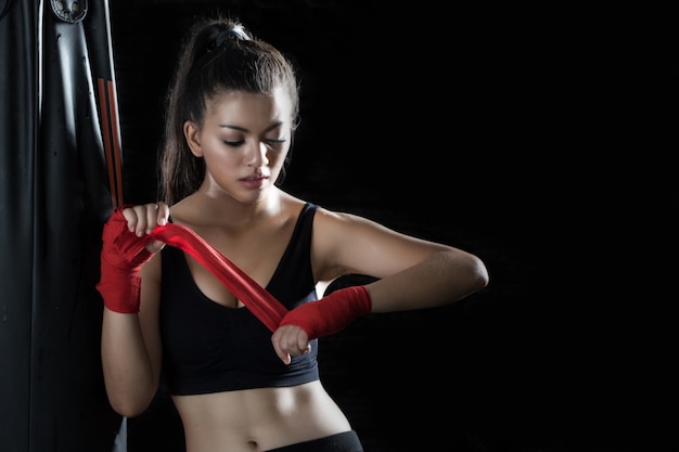 La giovane donna è in piedi, avvolta in un panno per le mani per praticare la boxe in palestra.