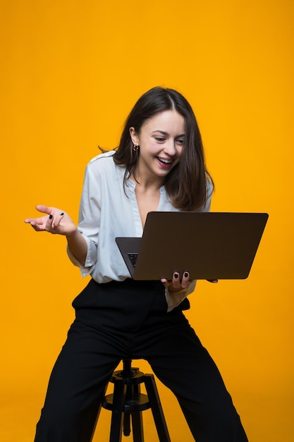 A young woman is surprised by the information on the laptop screen on a yellow background