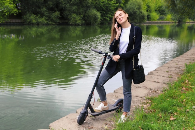 A young woman is talking on the phone next to an electric scooter in the parkWalking around the city