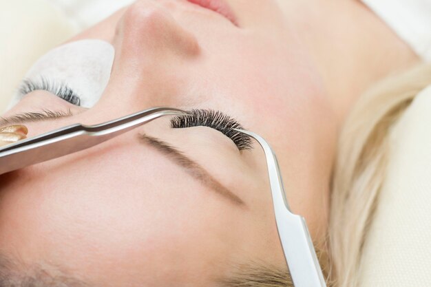 Young woman is undergoing a close-up eyelash extension procedure. Eyelash extension tweezers