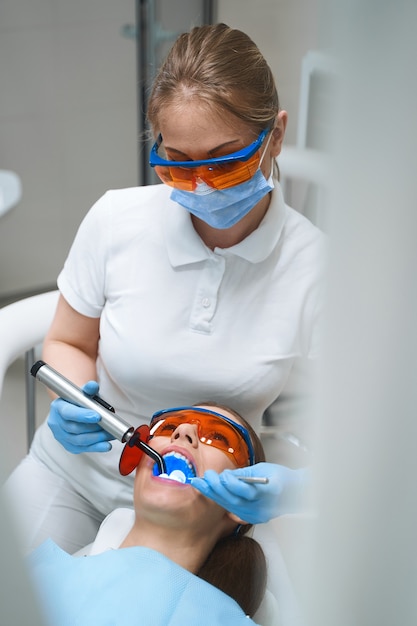 Young woman is visiting dental clinic for curing caries and putting filling with specialist assistance