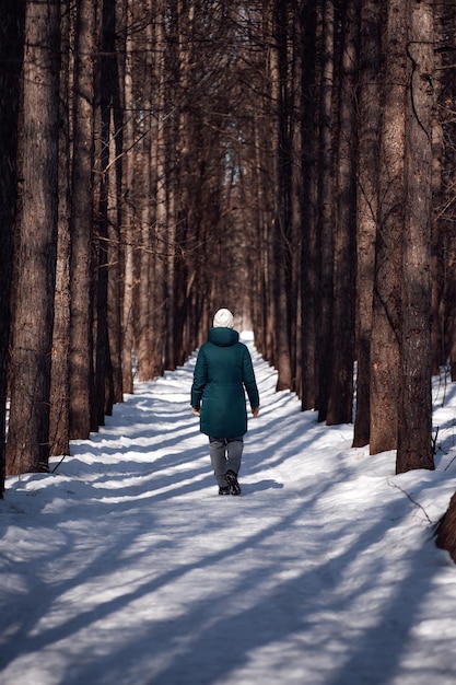 若い女性が雪に覆われた森の中の冬の道を歩いている緑の若い女性...