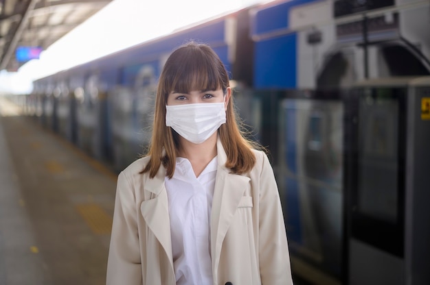 한 젊은 여성이 지하철, covid-19 보호, 안전 여행, 뉴노멀, 사회적 거리, 안전 교통, 전염병 개념 아래 여행에서 보호 마스크를 쓰고 있습니다.