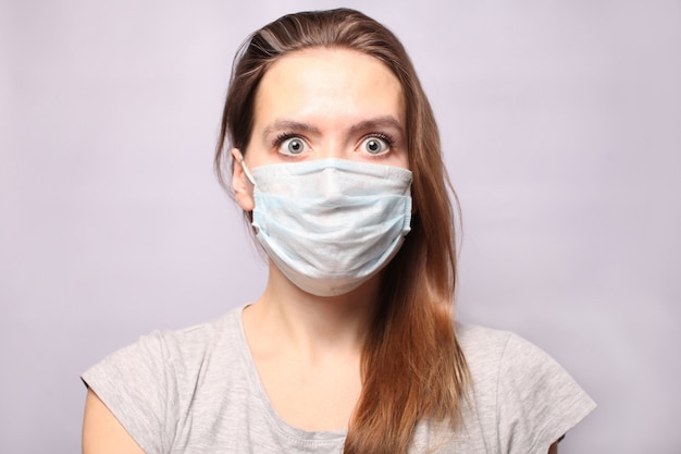 젊은 여자가 호흡기 보호 마스크를 착용하고 있습니다. 씹는 껌은 두려움으로 회색으로 변했고 눈이 크게 무섭게 보입니다. 독감 전염병, 먼지 알레르기. 코로나 바이러스 2019 nCoV.